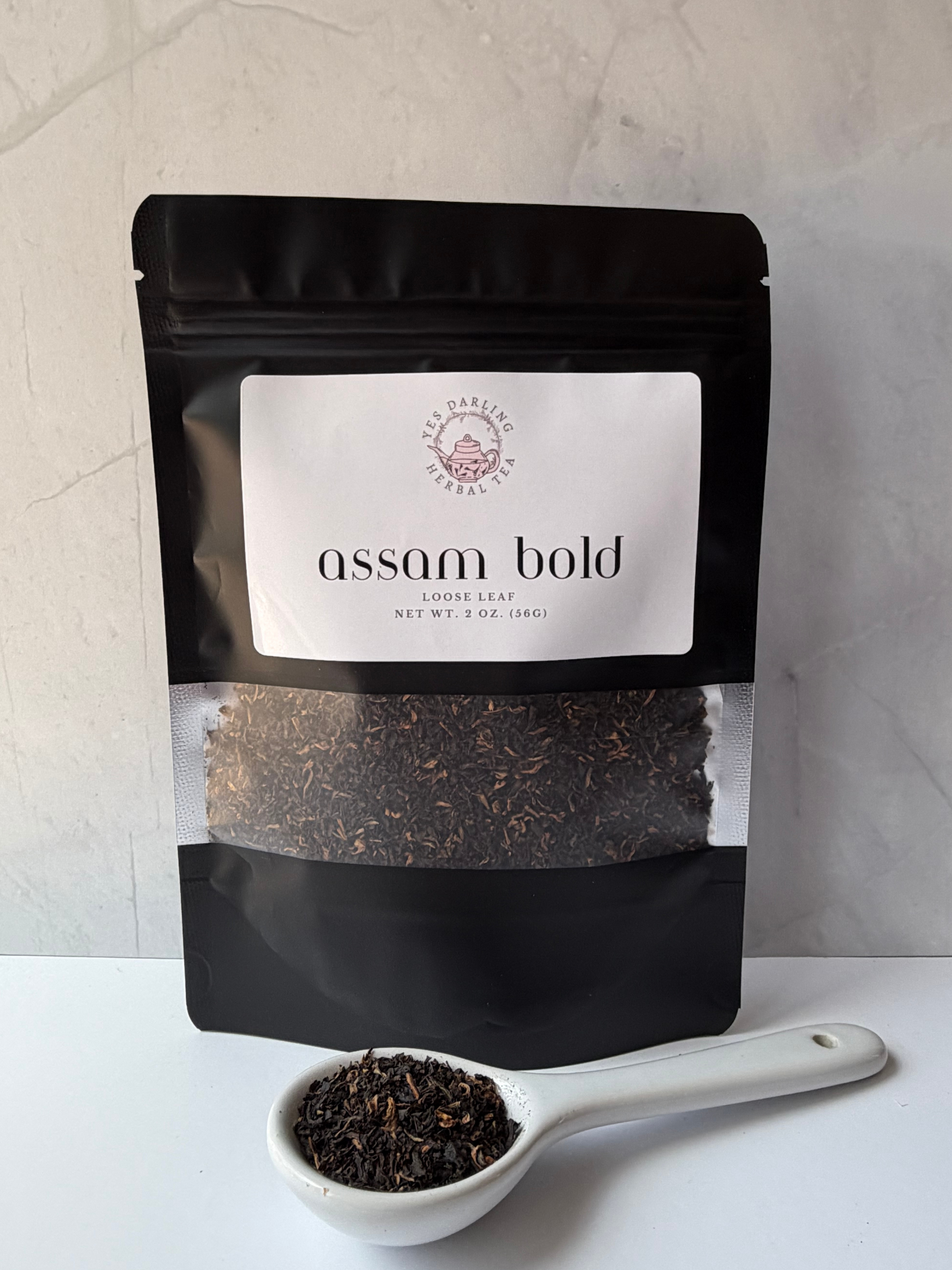 Tea package labeled 'Assam Bold' with a spoonful of tea leaves on a light background
