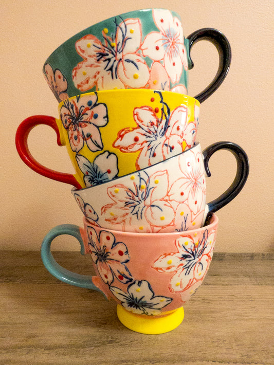 Four assorted tea mugs colored teal, yellow, pink, and white.